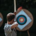 Junger Mann, der mit Bogen auf Zielscheibe zielt