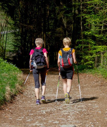 Zwei Frauen mit Nordic-Walking-Stöcken durch Wald laufend