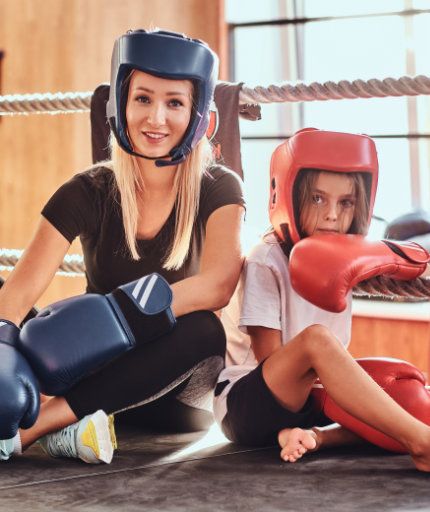 Trainerin mit Kind in Kickboxmontur im Ring sitzend